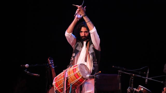 Man on stage with a traditional drum, hands in the air clapping