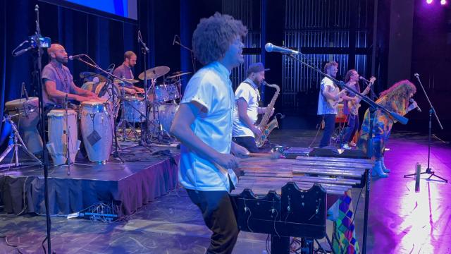 Image of a band performing on stage featuring a man playing the marimba.