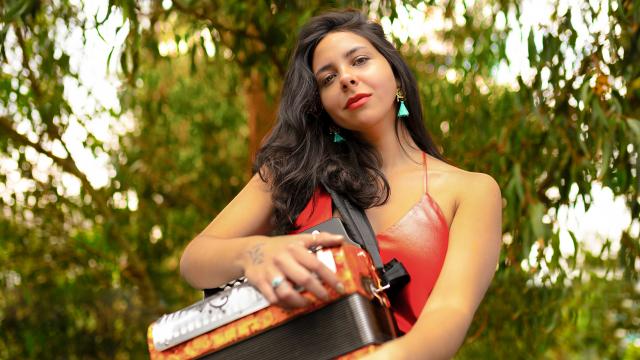 Diana Burco by Jose Cardona Woman holding an accordion in front of green foliage