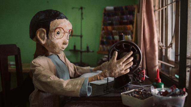 A puppet sitting at a table adjusting a sewing machine