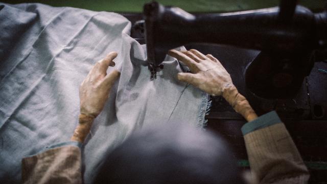 Two puppet hands feeding fabric through a sewing machine