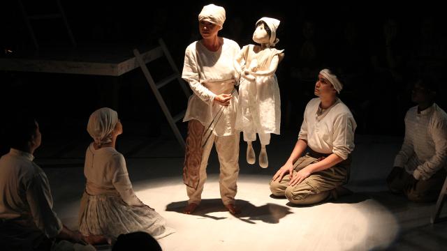 Tanghalang Pilipino A group of people, all wearing white, sitting around someone holding a small puppet