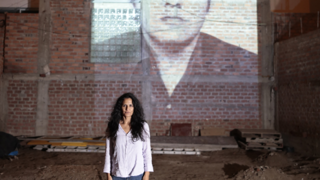 Woman standing in front of a brick wall, with an image of a man projected onto it