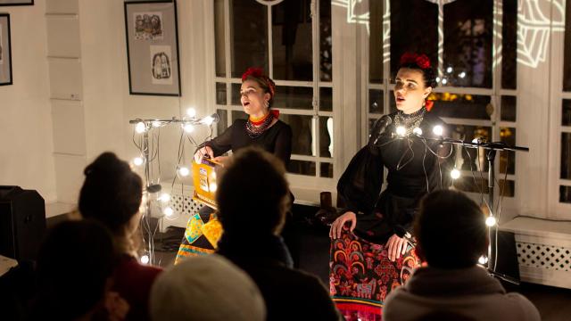 Two women perform in front of a crowd, lit by Christmas lights