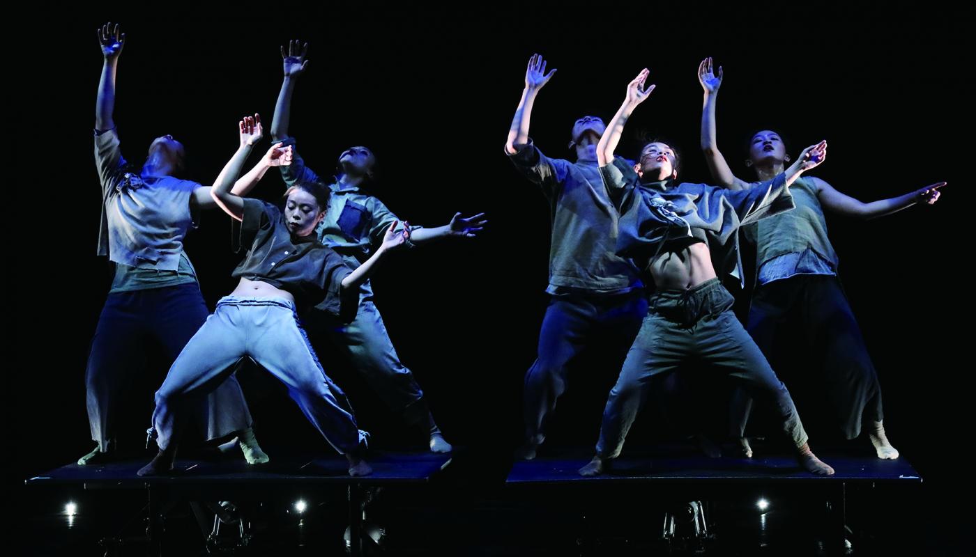 Dancers on stage in gray outfits, leaning backwards with their hands in the air