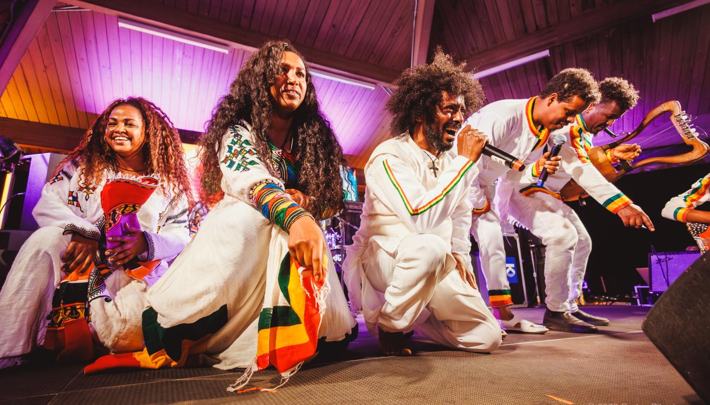 Five dancers and musicians in Ethiopian costumes kneel towards the edge of a stage