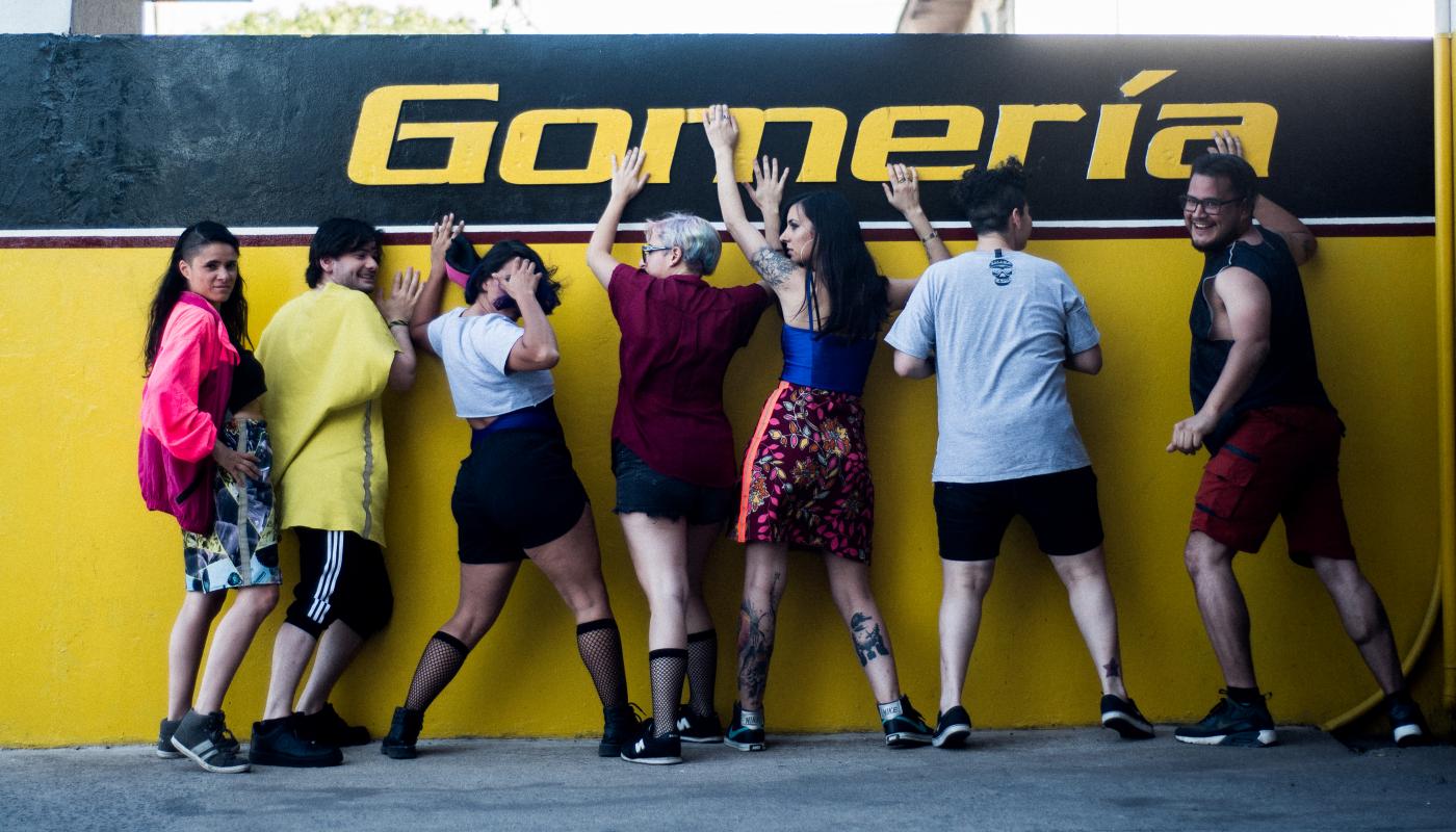 Seven people posting against a yellow wall, turning back towards the camera with silly faces