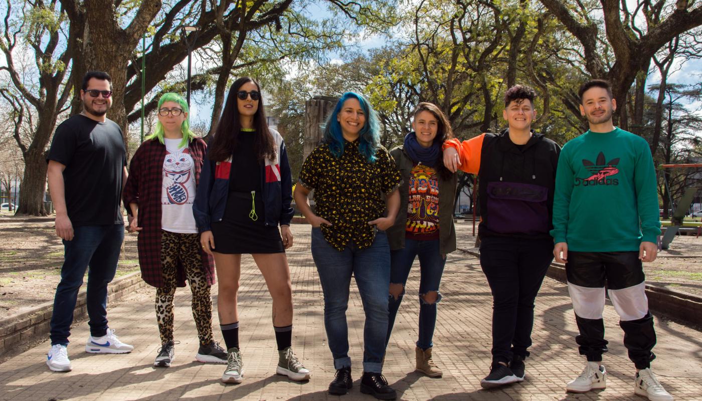 Seven people stand in a line with large trees framing them from the background