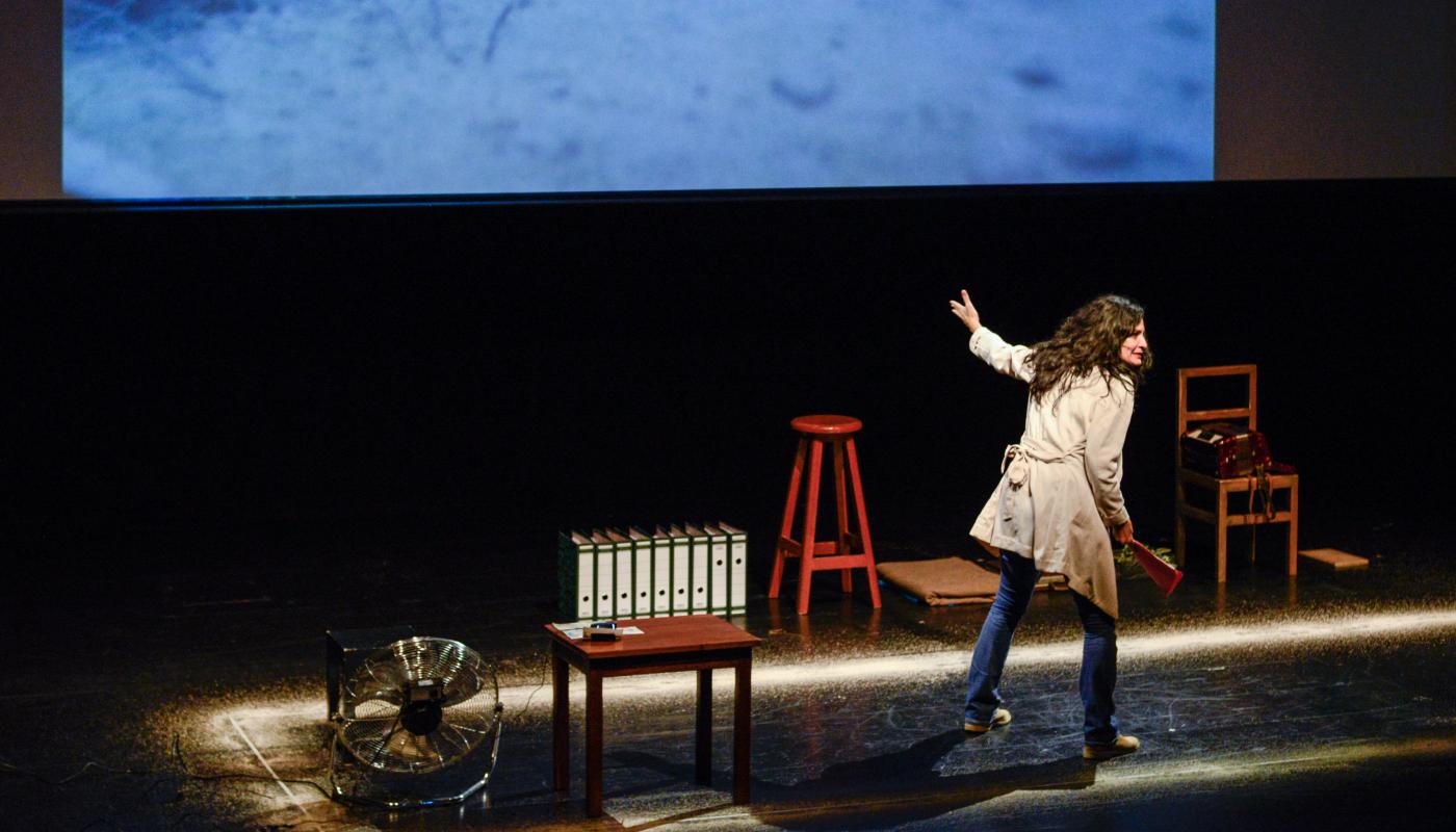 A woman on a stage, pointing towards a projection screen