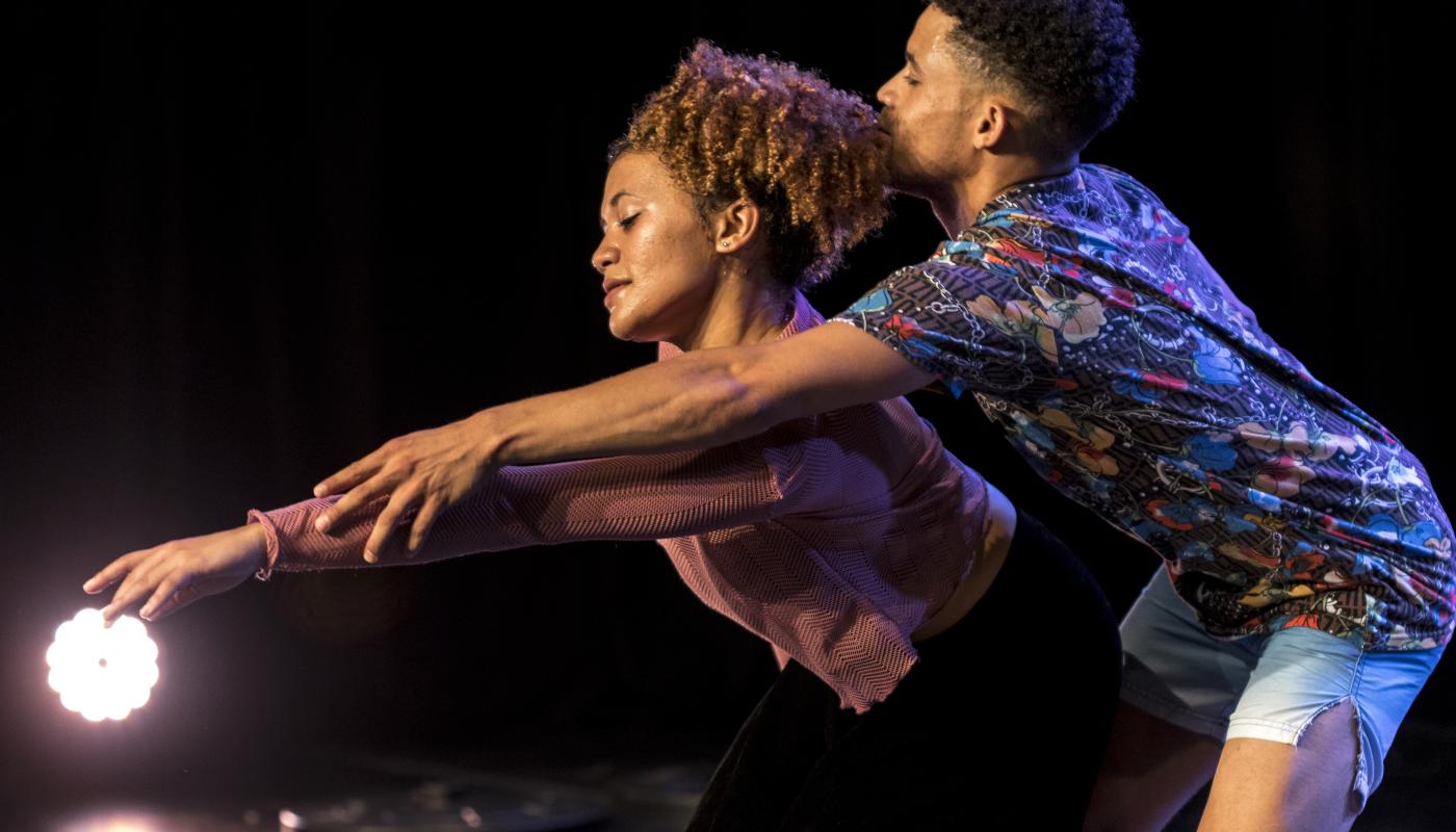 Two dancers reach outwards towards a white light