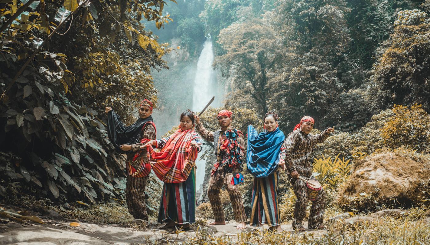 Five indigenous Filipino performers stand in front of a waterfall