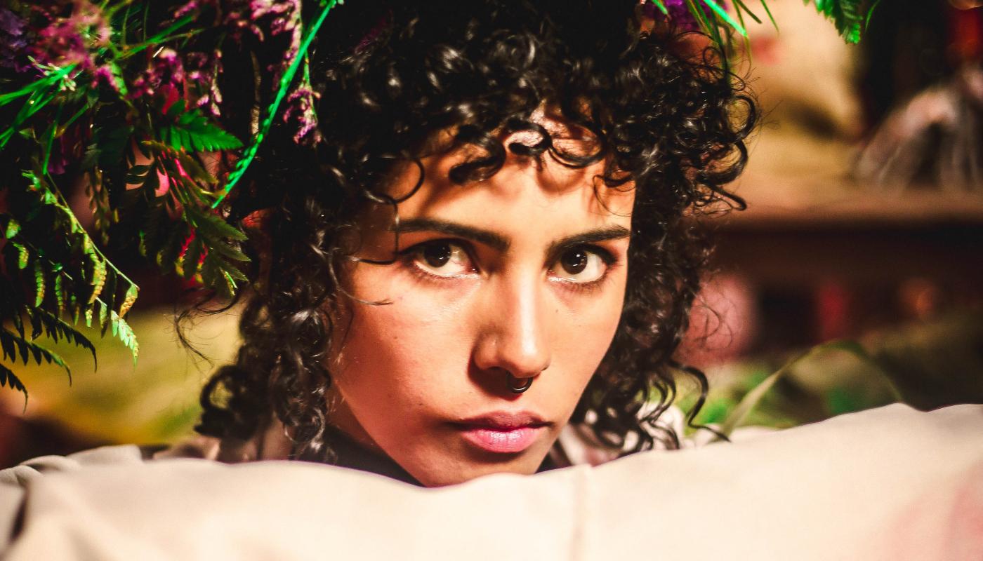 A women with flowers in her hair and large sleeves posed and looking directly at the camera.