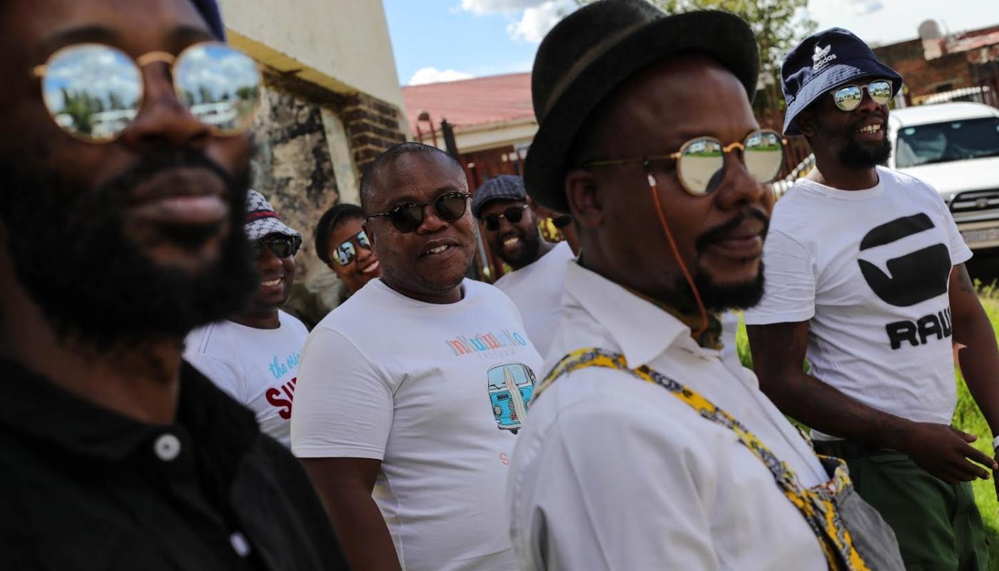 A group of men wearing sunglasses, walking through the frame