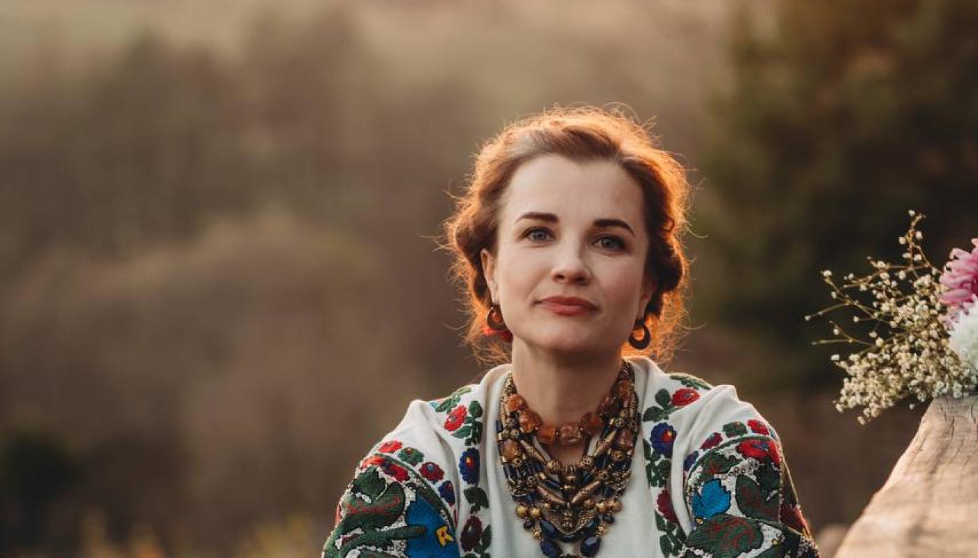 Maria of Kurbasy, photo by Liuba Chornenjka A woman sitting on a bench with her knees up close to her chest, backlit by the sun