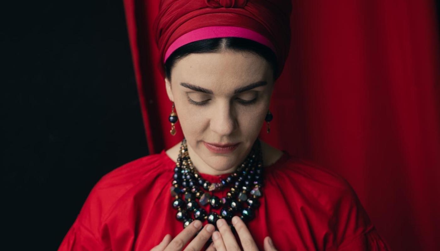 Natalia of Kurbasy, photo by Maria Raymers A woman in traditional Ukrainian clothing, looking down with her hands on her chest