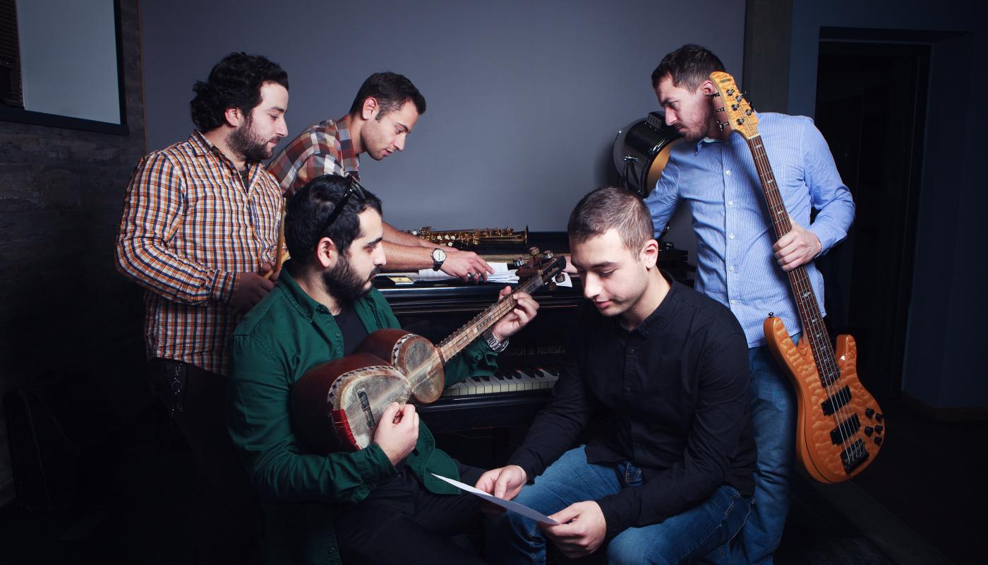 Five musicians with instruments, posing around a piano