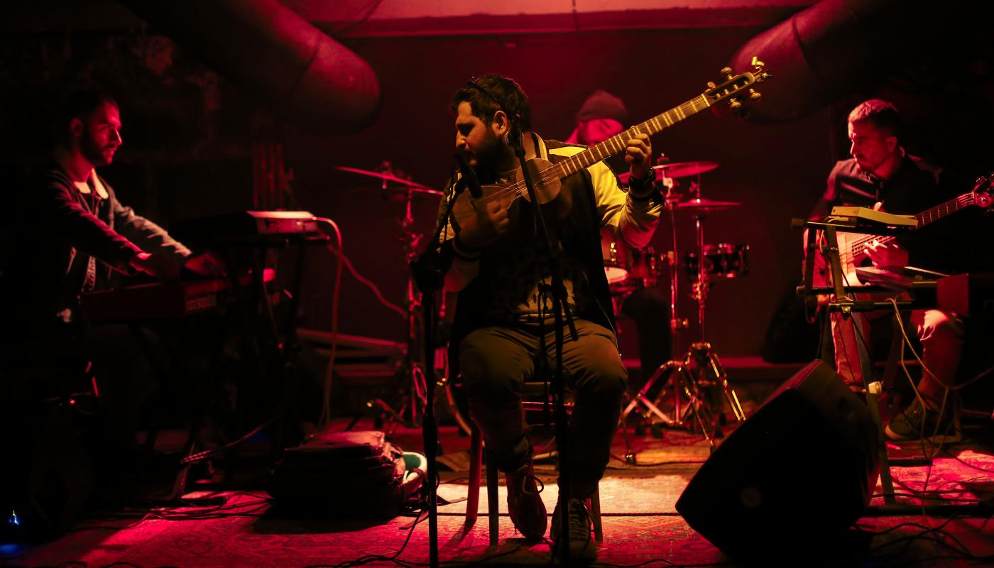 Three musicians on a stage playing instruments, illuminated by red light