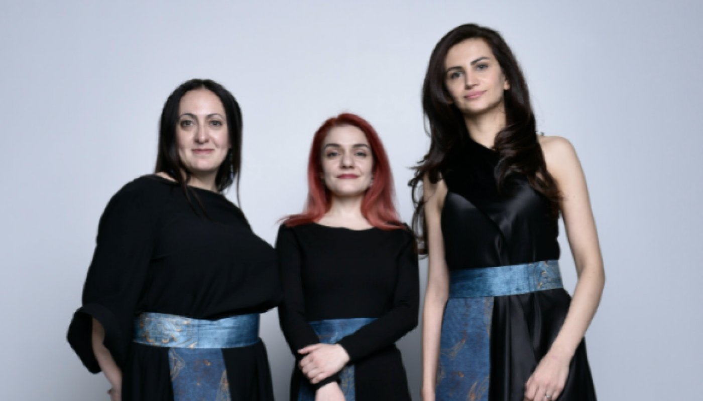 Three women in black dresses with colorful sashes