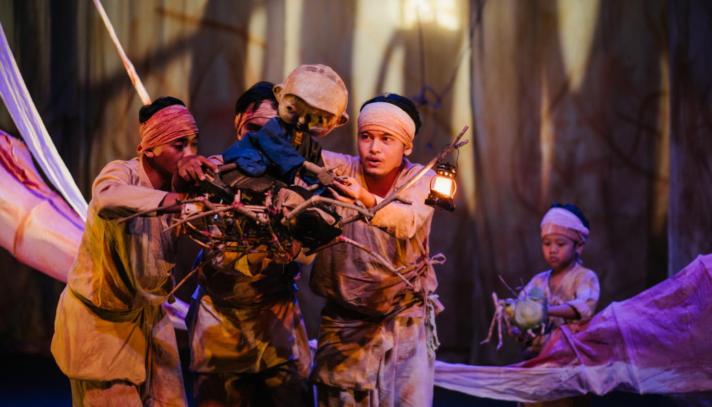 Three puppeteers move a puppet across a stage