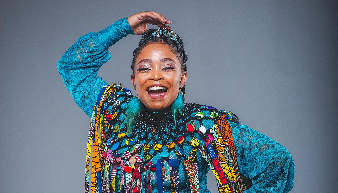 A black woman poses for the camera wearing brightly colored clothes.