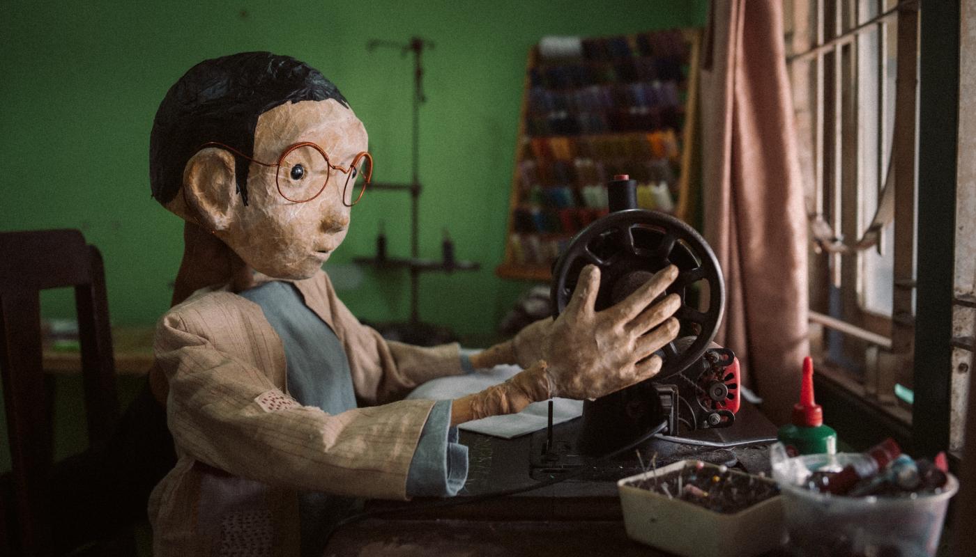 A puppet sitting at a table adjusting a sewing machine