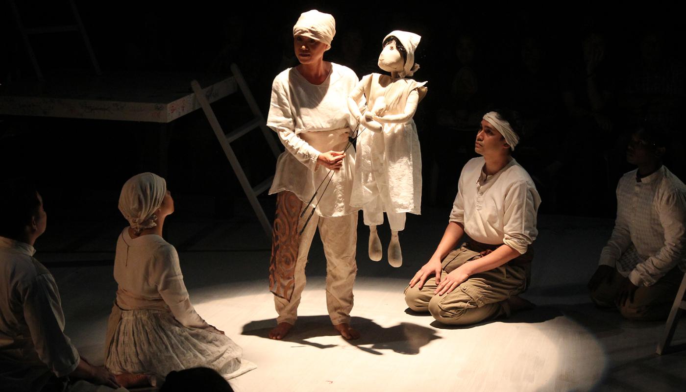 A group of people, all wearing white, sitting around someone holding a small puppet