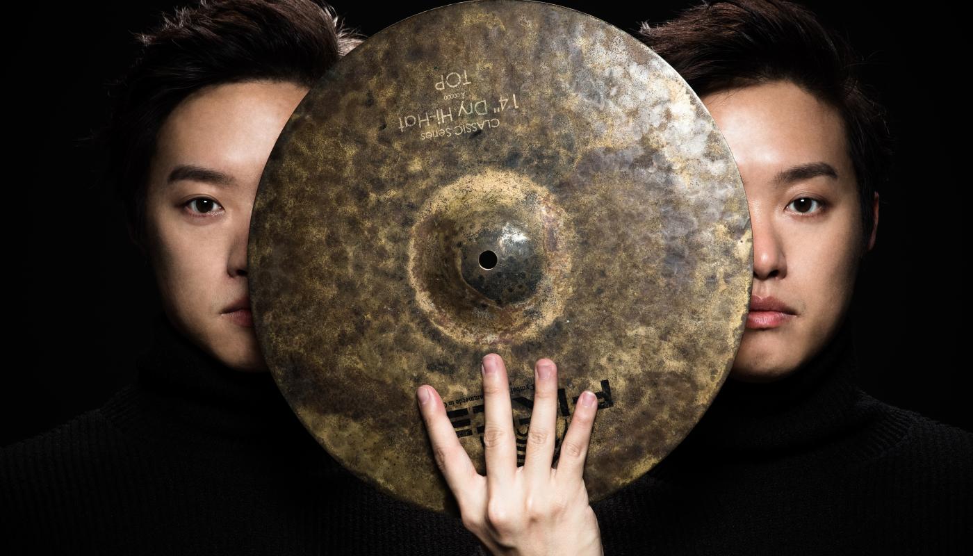Two men holding a cymbal between their faces