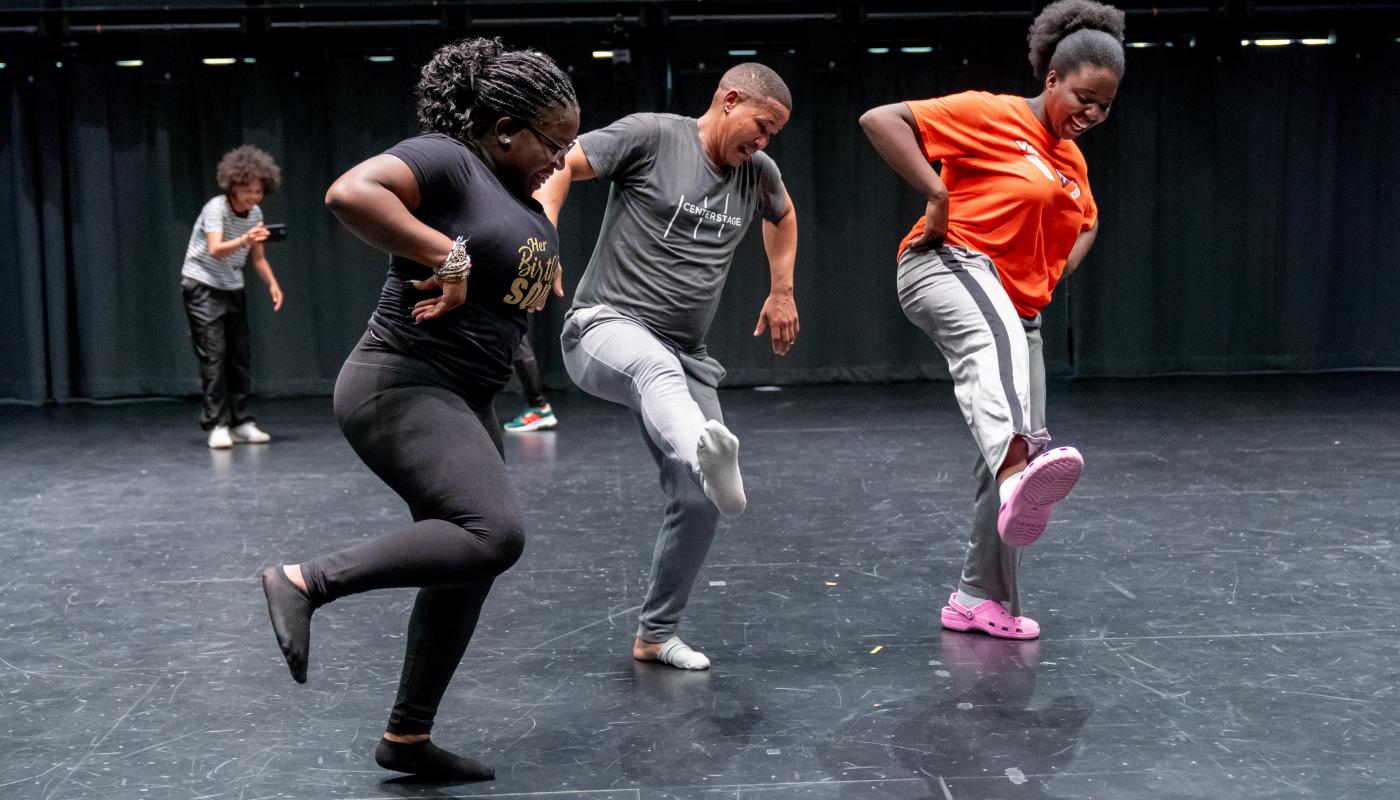 One man and two women dance together with their right leg in the air