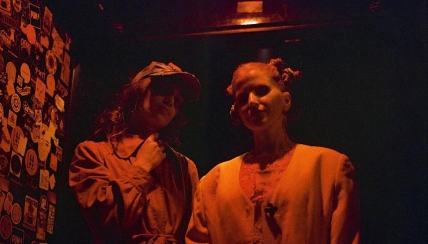 Two women in a dark room illuminated by an orange light. 