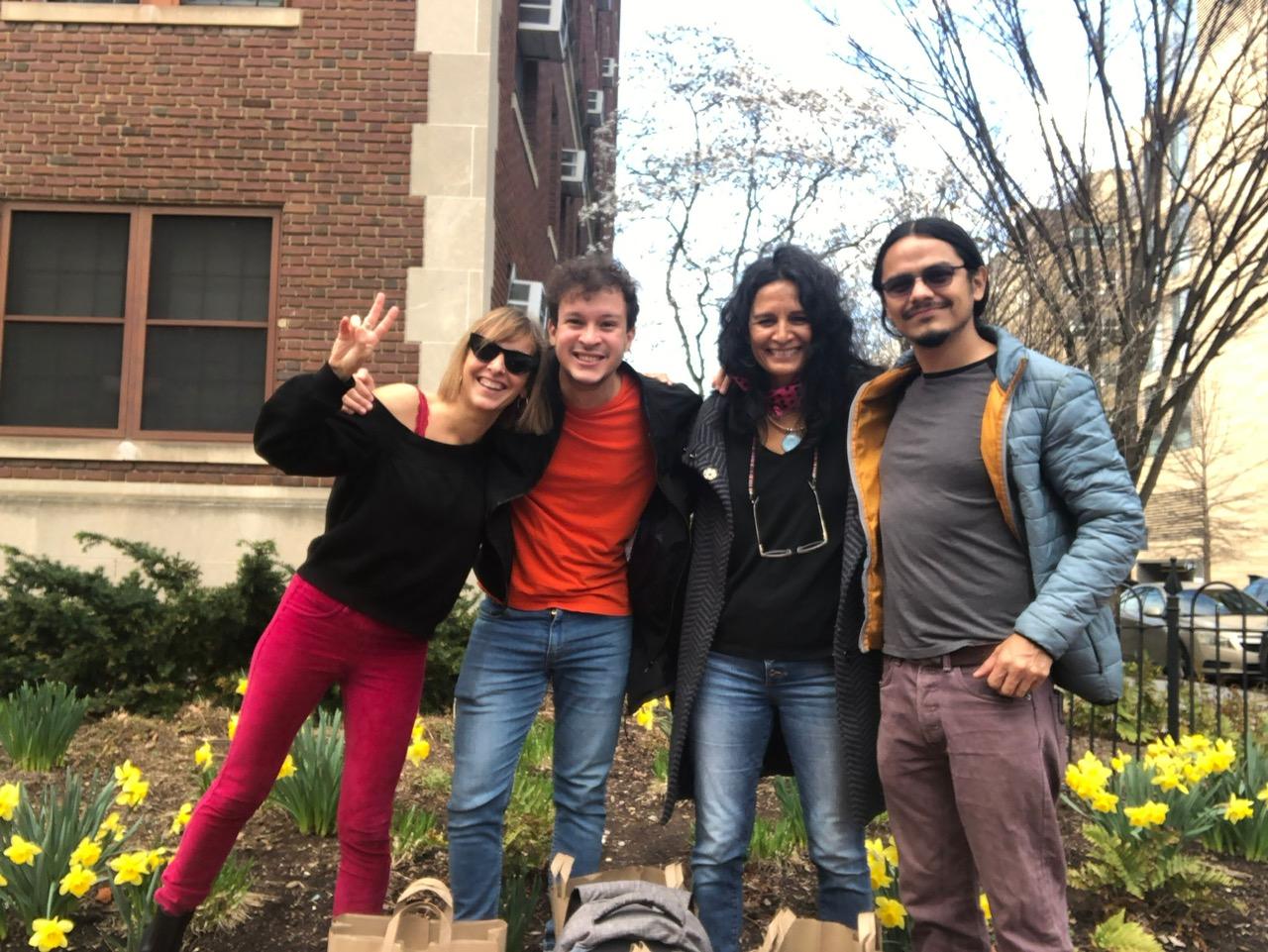 Four people posing in front of a building with daffodils