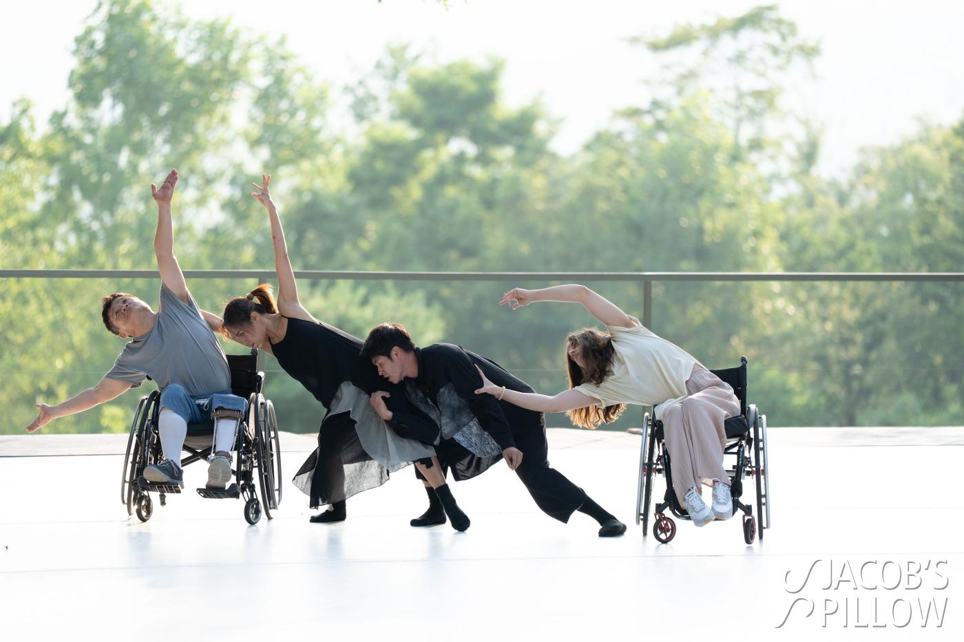 Four performers dance together on an outdoor stage