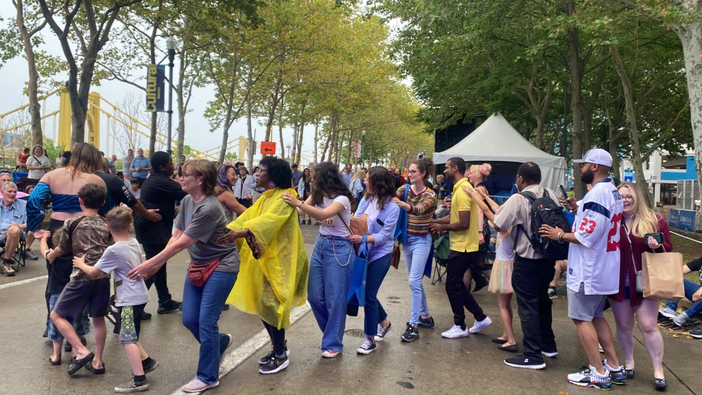 A large group of people form a conga dance line on a street