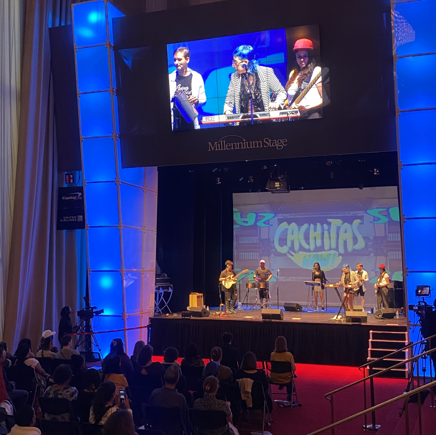 Cachitas Now! in Washington DC by Aketzali Vazquez A band performs on a stage with several rows of chairs filled with audience members