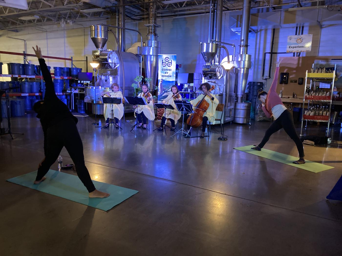 Four women musicians perform while people do yoga