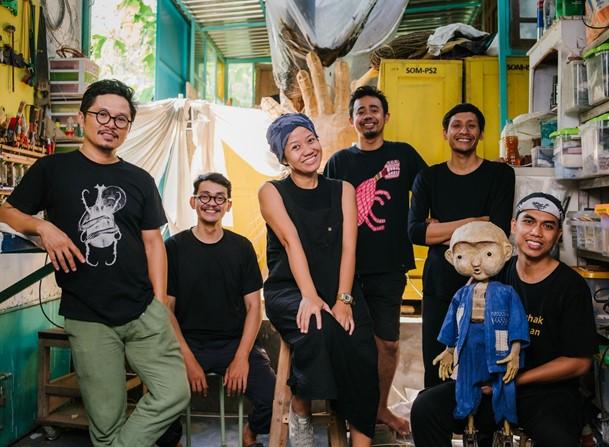 Papermoon Puppet Theatre in their studio by Josh Kohn Six men and women, both sitting and standing, posing for the camera in their art studio, one person is holding a puppet.