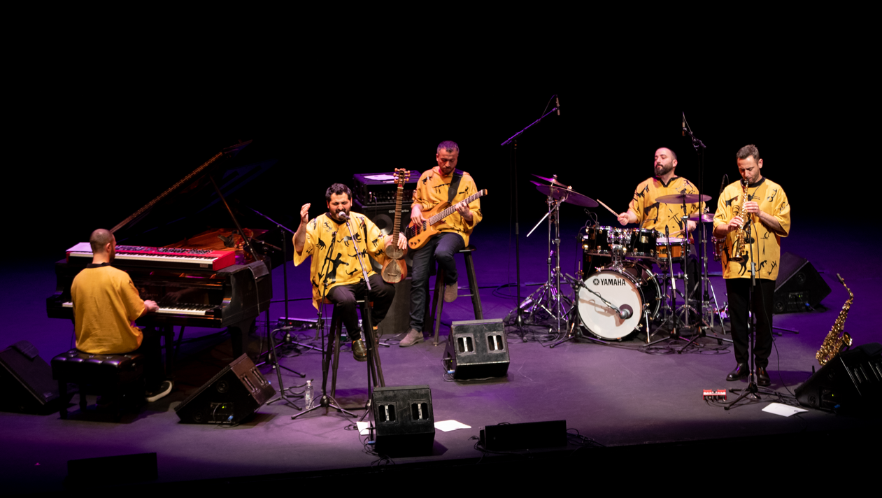 A group of musicians perform on stage in yellow Armenian outfits