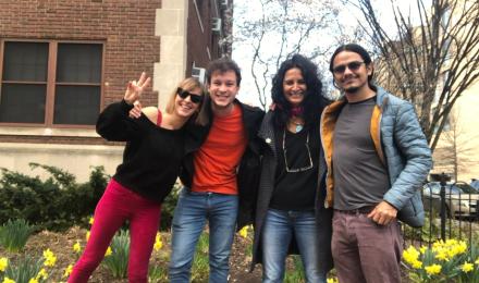 Four people posing in front of a building with daffodils