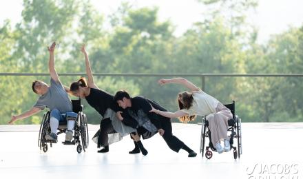 Four performers dance together on an outdoor stage