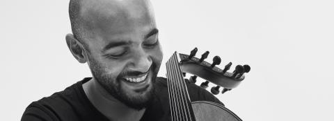 A black and white portrait of a man in a black t-shirt holding an oud.