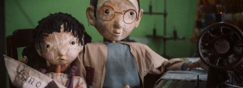 Two puppets looking at the camera, one with a sewing machine and one with a small boat