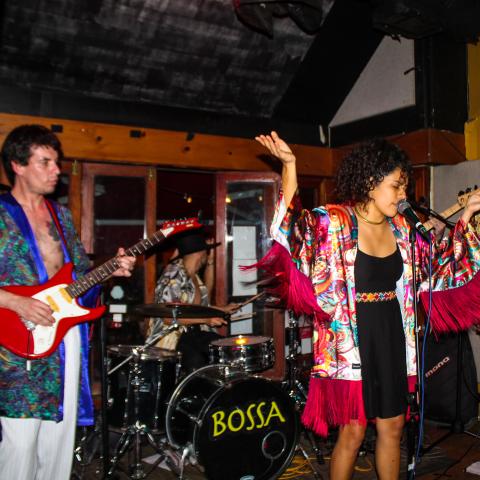 A group of musicians dressed in psychedelic robes perform on stage at a nightclub.
