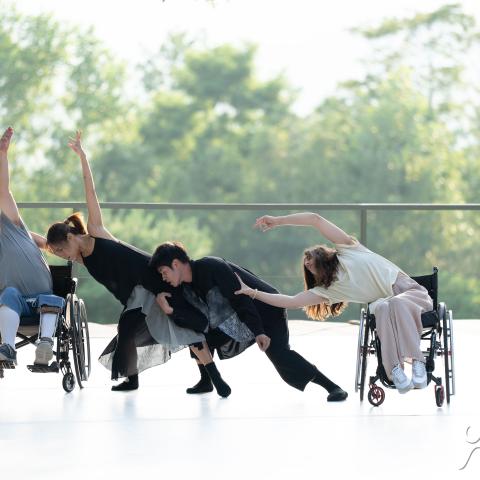 Four performers dance together on an outdoor stage