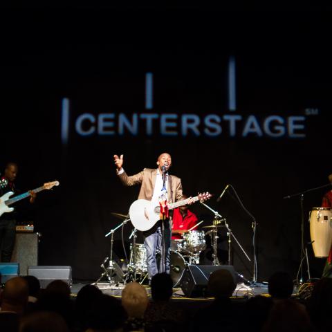 A band performing on a stage, lead singer with their arm out stretched