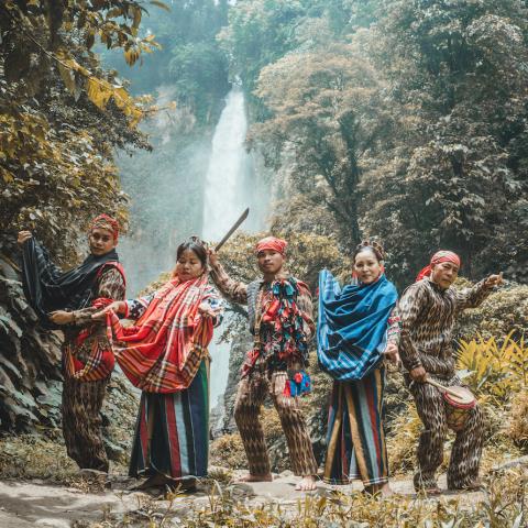 Five indigenous Filipino performers stand in front of a waterfall