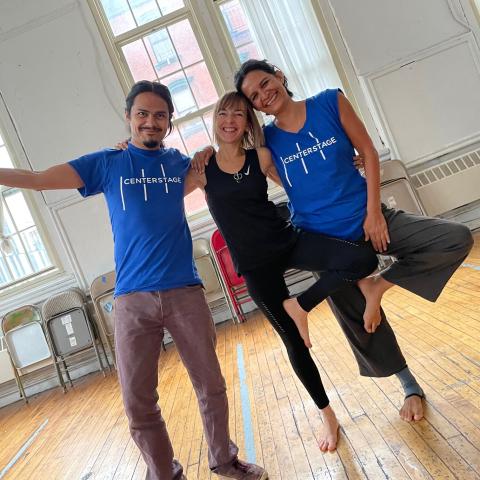 In a dance studio, three adults pose with arms around one another. 