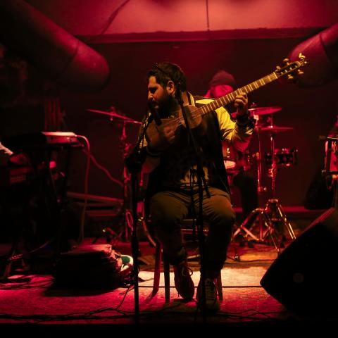 Three musicians on a stage playing instruments, illuminated by red light