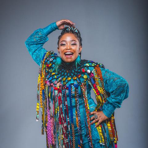 A black woman poses for the camera wearing brightly colored clothes.