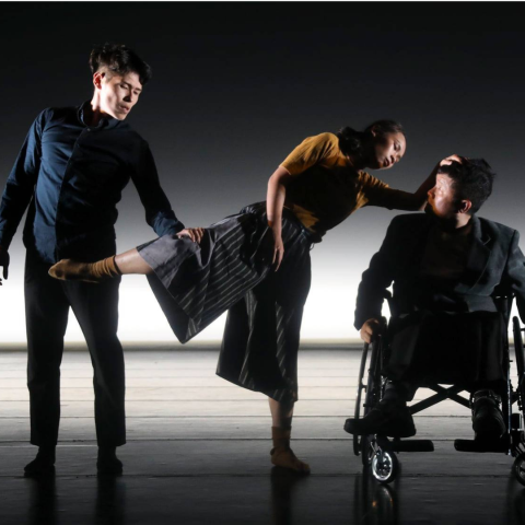 A man next to a woman who is standing on one leg and leaning on another man in a wheelchair